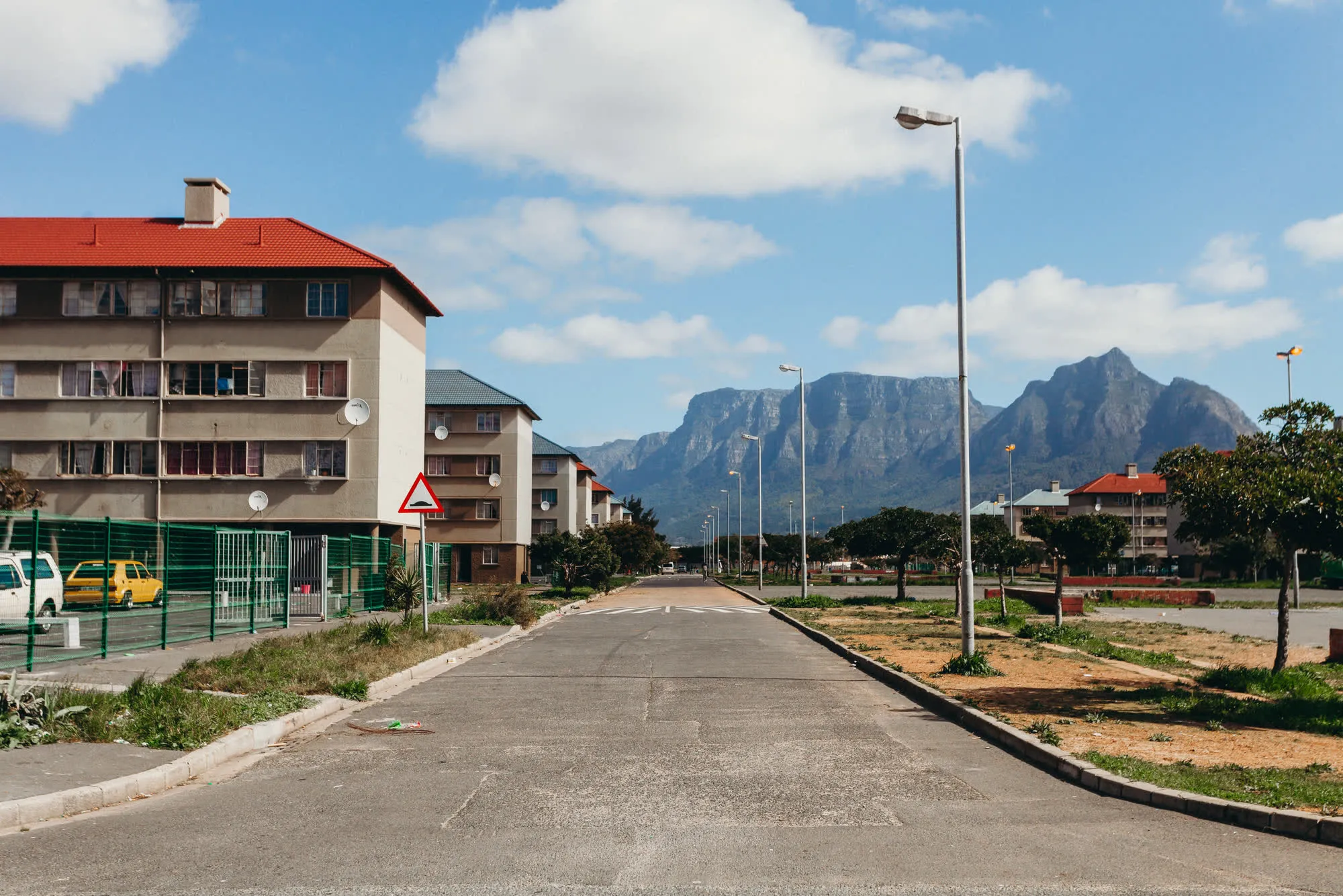 A quiet Athlone street of flat-roofed apartment blocks under Table Mountain, trees lining the road